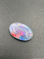 Oval opal gemstone displaying vibrant play of colors on dark background.