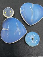 Four blue and white opaline gemstones on black background, including two heart shapes and two round stones showing reflective light