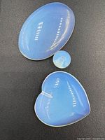 Three blue opaline cabochon cut stones: large oval, heart-shaped, and small round with glossy surfaces.