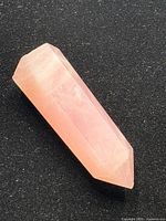 Rose quartz crystal point with polished facets and pink translucent color, resting on a black background.