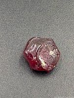 Close-up image showing the rough ruby gemstone with natural crystalline facets and reddish coloration.