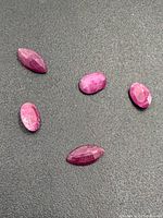 Five faceted ruby gemstones in various cuts and shades of red arranged on black background.