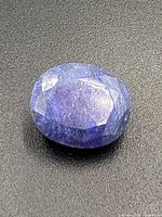 Close-up of the sapphire gemstone showing a medium blue color with faceted oval cut and visible inclusions.