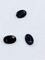 Three oval blue sapphire gemstones placed on a white surface for clear viewing of their color and size.