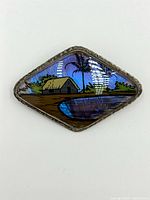 Diamond-shaped sterling silver brooch showing detailed reverse painted tropical scene including hut, palm trees, water, and 'PANAMA' text