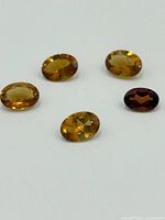 Five oval faceted topaz gemstones in varied shades of yellow and brown placed on white background