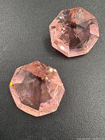 Close-up of two pink octagon-cut topaz gemstones on a black surface showing their facets and color.