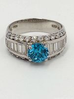 Front view of sterling silver ring with round blue topaz center stone and surrounding clear accent stones.