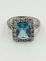 Front view showing rectangular blue topaz center stone surrounded by clear stones on sterling silver band.