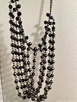 Close-up photo of the four strands of small black rhinestones linked on dark metal chain, showing the detailed faceted stones and links.