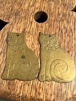 Close-up image of two brass cat wall decorations with etched details and patina