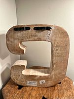 Wooden letter C viewed from the back showing two hooks for hanging and a label stating 'Made in India'. The natural wood texture is visible.