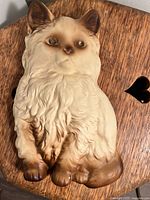 Front view of cream and brown cat chalkware figurine with detailed fur and greenish eyes on wooden surface.