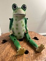 Green ceramic frog figurine sitting on a wooden surface with heart-shaped cutouts, showing front and angled front views.
