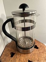 French press coffee maker showing glass carafe, stainless steel lid, plunger and strainer with black plastic handle and base.