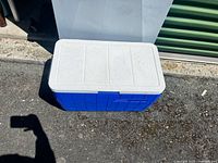 Blue and white camping cooler placed on the ground outside against a white backdrop showing front and top view.