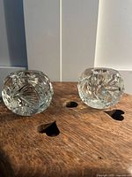 Front angled photo showing both clear crystal candle holders on a wooden surface with heart cutouts.