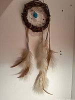 Full view of dream catcher showing round wooden frame, string web with blue stone in center, and hanging feathers