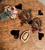 Photo showing ceramic ring with pink stone, pair of ornate earrings with red beads, and ceramic pendant on wooden heart-patterned surface