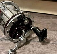 Side view of a vintage metal fishing reel showing handle and spool