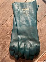 Pair of green Horizon PVC coated work gloves laid flat on a wooden floor, showing full gloves and branding on cuffs.