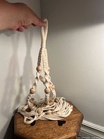 Macrame plant pot holder held by a hand showing the top loop and braided design with wooden beads.