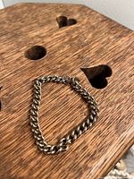 Metal chain bracelet laid on a wooden surface with heart and circle cutouts, showing the entire chain and the loop clasp.