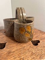 Speckled brown pottery tri-holder showing two compartments and yellow-orange flower details on visible sides, with sturdy handle between compartments.