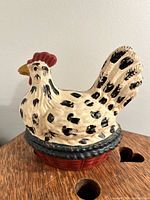 Front and side views of the ceramic rooster figurine showing its color and texture on a small wooden table.