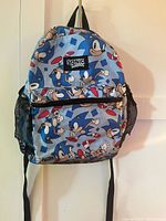 Front view of blue Sonic the Hedgehog backpack with multiple Sonic character images and front zip pocket.