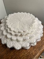 Stack of white stretchy knit doilies in various sizes on wooden surface