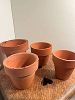 Four small terracotta pots arranged on wooden surface showing chips and worn edges