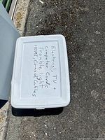White lid of plastic container with handwritten list of contents including electrical, TV, computer cords, coaxial cables, and HDMI cords.