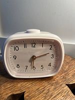 Front view of vintage white plastic alarm clock showing the face with black numbers and gold hands on a white background.