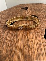 Full view of the gold tone beaded bracelet with central rhinestone detail lying flat on wood surface.