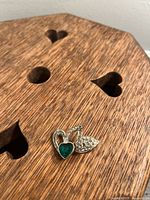Top view of the vintage heart-shaped silver-tone pin showing emerald green and clear rhinestones on a wooden surface with heart-shaped cutouts.