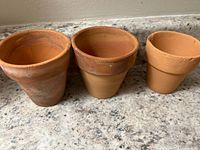 Three small vintage Italian terracotta pots on a speckled countertop. Each pot shows visible wear, discoloration, and small cracks from age and use.