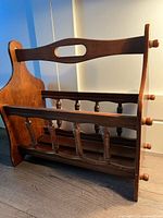 Full side angle view of the wooden vintage magazine rack showing spindle rails and cutout handle.