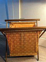 Front view of a vintage yarn holder with wooden frame and patterned fabric basket, showing wear and tear.