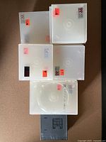 Top-down view of assorted white Video 99 CD/DVD cases and black Nintendo DS game cases stacked showing their translucent plastic material and red-orange stickers.