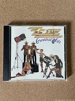 Front cover of ZZ Top Greatest Hits CD in jewel case, showing band members posing in studio setting with film equipment and lighting.