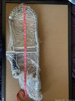 Chef style kitchen faucet wrapped in protective plastic wrap, laid flat on a surface with measuring tape extended alongside to show length.