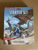 Front cover of the D&D Starter Set box, featuring a large blue dragon and characters preparing to fight. The box states it's for 2-6 players, age 12+.