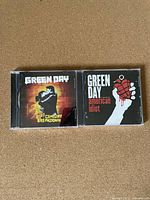 Front covers of Green Day CDs '21st Century Breakdown' and 'American Idiot' laid side by side.