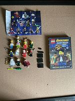 Top-down photo displaying the Lego Adventures of Clutch Powers DVD, 11 minifigures arranged in 3 rows on a corkboard surface along with 3 black platform attachments.