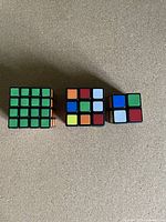 Photo shows three Rubik's cubes of sizes 2x2, 3x3, and 4x4 with standard color stickers, set on a flat surface.