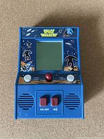 Front view of the blue Space Invaders mini arcade game turned off, showing artwork, buttons, joystick, and speakers.