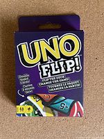 Photo of UNO Flip card game box showing brand name, colorful card illustrations and player/age details.