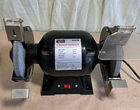 Front view of bench grinder showing wheels, base and damaged shields