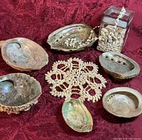 Group shot of six abalone shells, woven shell placemat, glass jar with small shells